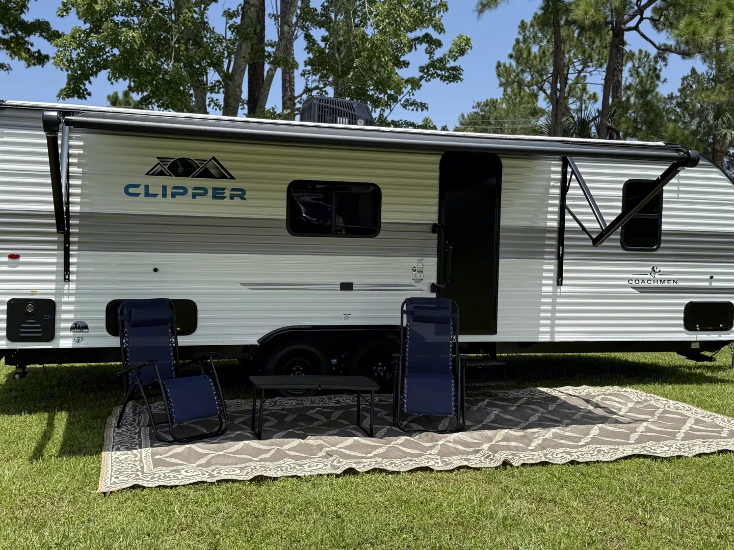 Coachmen Clipper exterior with awning, chairs, and mat